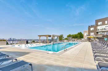A large outdoor swimming pool with sun loungers and a building in the background.